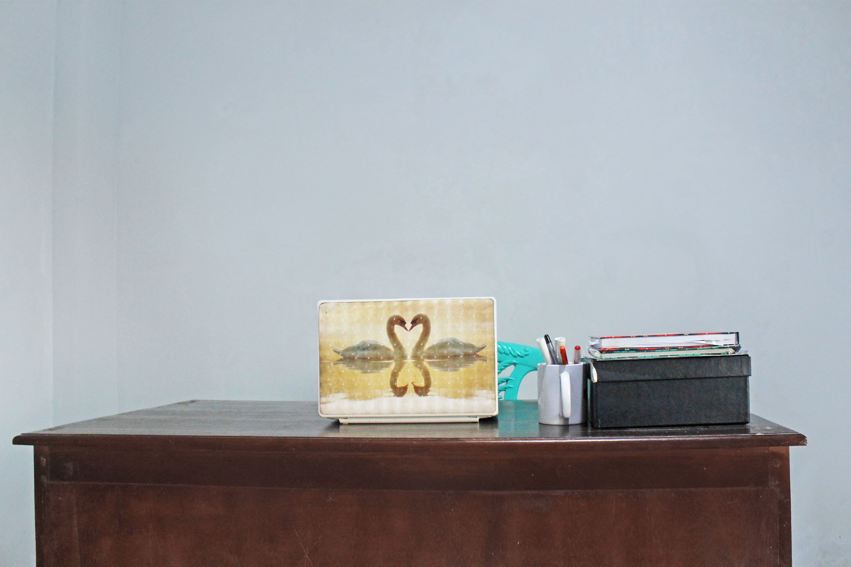 A wooden desk with a laptop featuring a swan design, a teal chair, and a black box with papers.