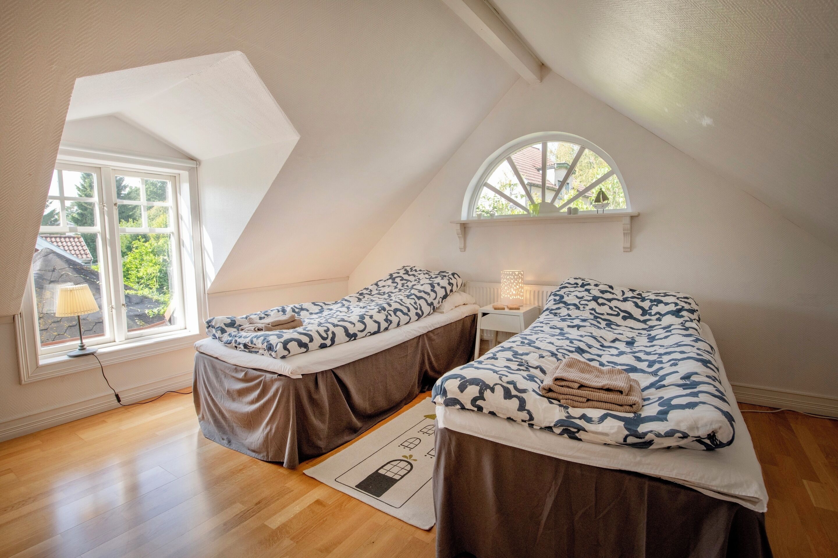 A small, well-lit room with two beds, a window, and a view of greenery outside.