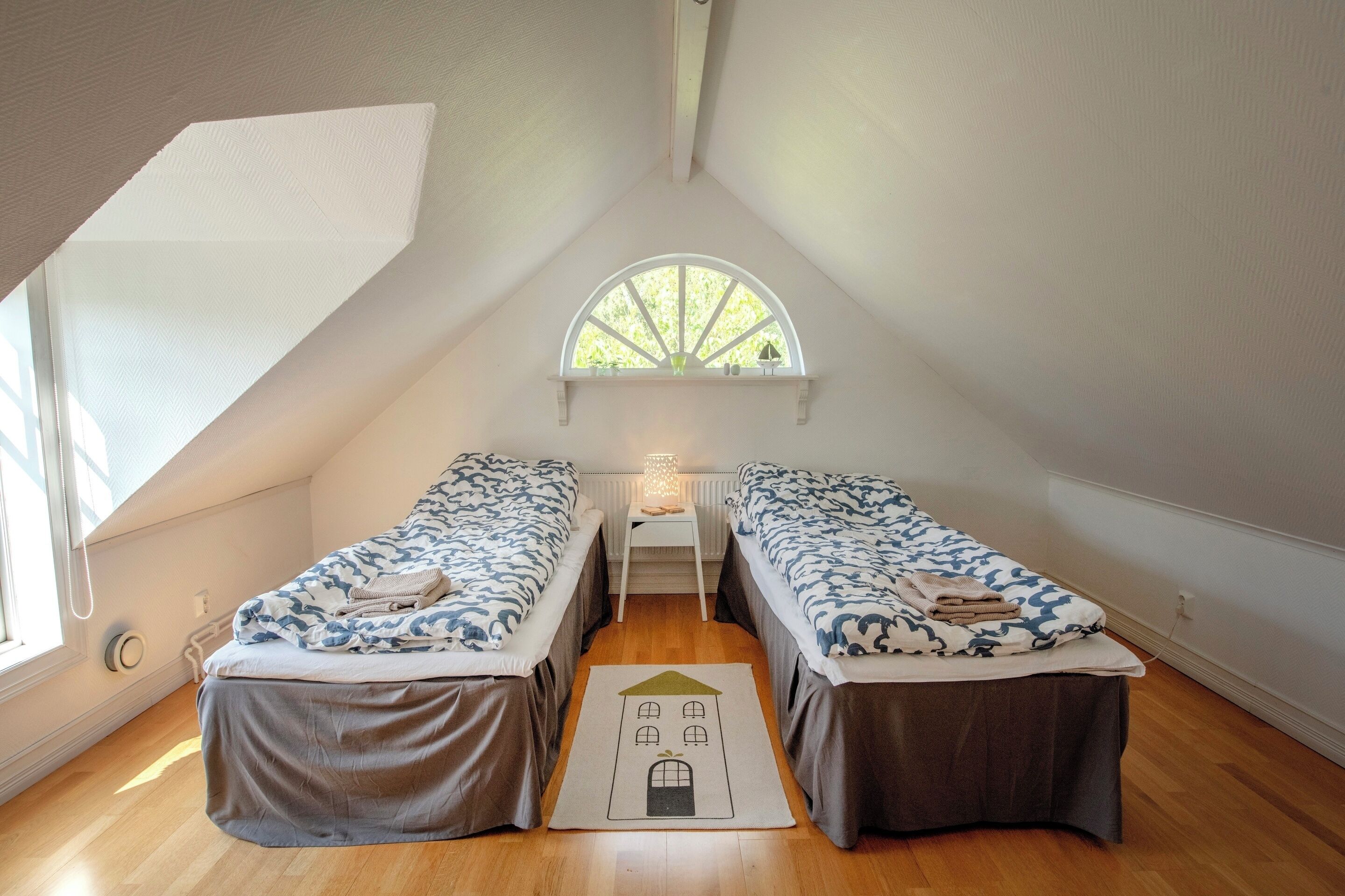 Un dormitorio de ático pequeño y triangular con dos camas, una ventana y un radiador.