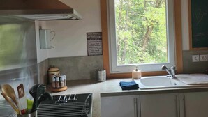 Una cocina con techo de madera, una ventana con vistas a árboles, un lavamanos y armarios.