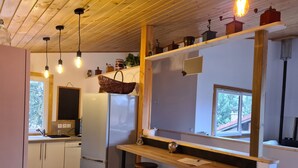 Una cocina compacta con refrigerador, mostrador de bar de madera, taburetes e iluminación colgante.