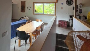 Un interior moderno con techo de madera, un comedor con una mesa larga y sillas, una cocina con estufa y un amplio ventanal que ofrece vistas a zonas verdes.
