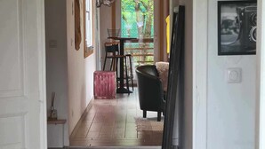 Un pasillo con suelo de madera que conduce a un comedor con una mesa, sillas y una maleta roja, además de una silla negra.