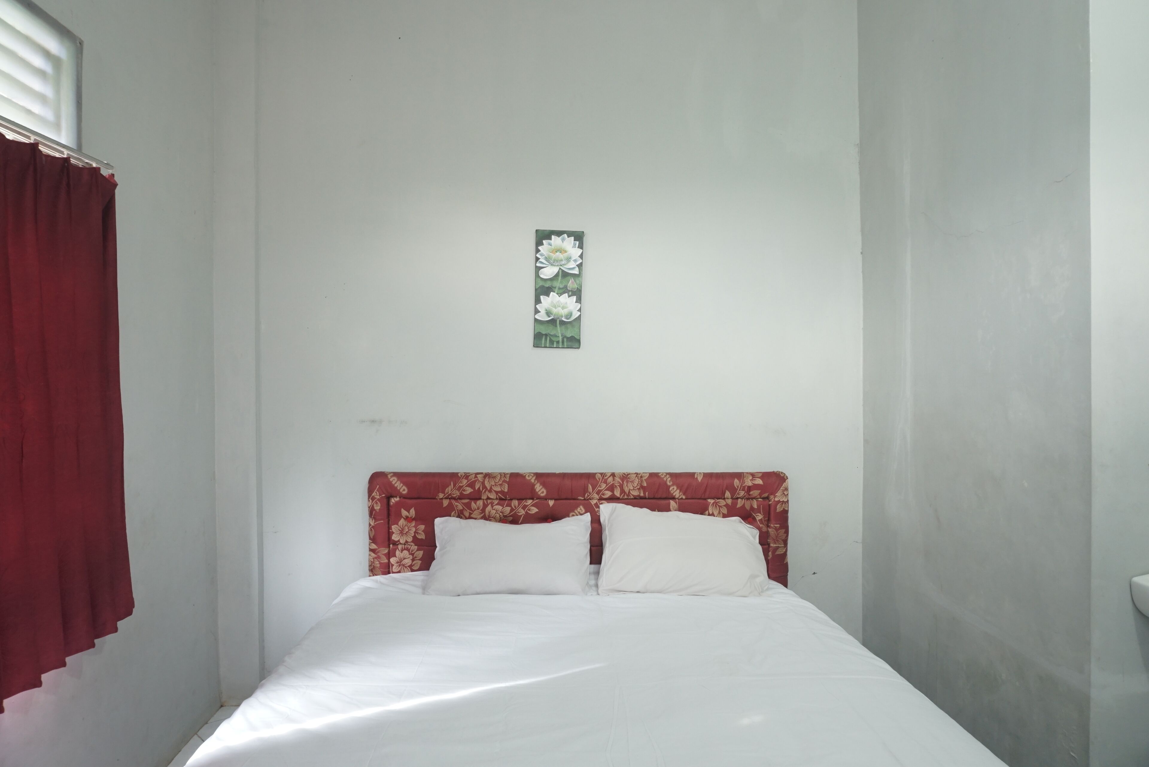 A room with a bed, white bedding, a floral headboard, and a red curtain.