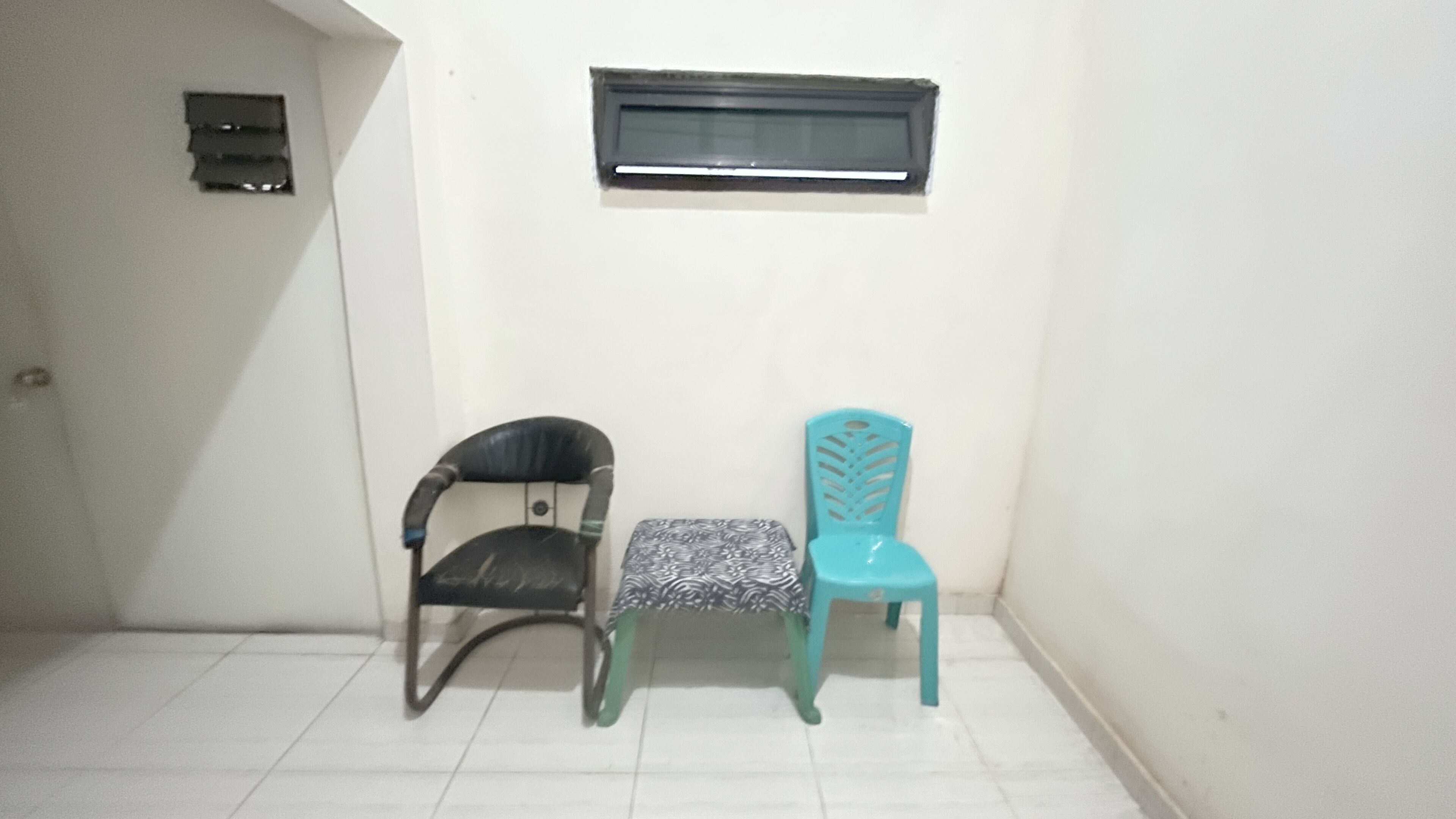 Une petite pièce avec deux chaises, une noire et une turquoise, et une fenêtre au-dessus.