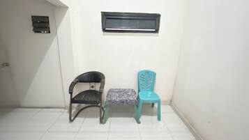 Une petite pièce avec deux chaises, une noire et une turquoise, et une fenêtre au-dessus.