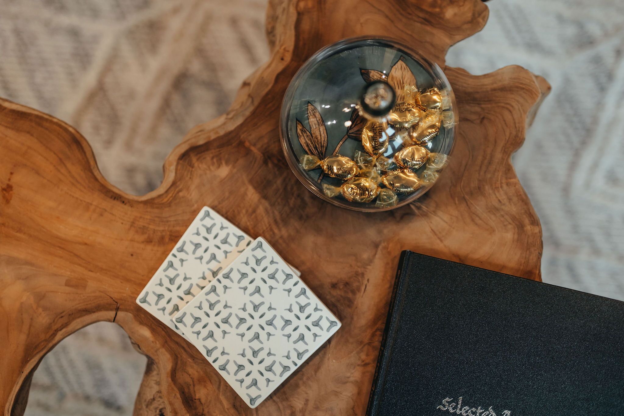 A wooden table with a glass bowl containing gold-colored items, a patterned card, and a black book.