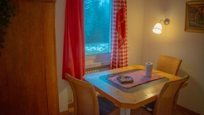 A dining area with a table, chairs, a window with curtains, a wall-mounted lamp, and a radiator. - Malixerhof (Churwalden)