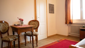 A room with a wooden table, two chairs, a red rug, a radiator, and a window with curtains. - Malixerhof (Churwalden)