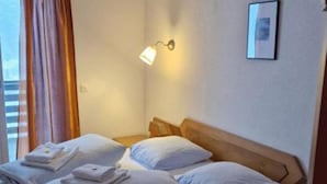 A hotel room with a wooden bed, white linens, a bedside lamp, a framed picture on the wall, and a window with curtains. - Malixerhof (Churwalden)