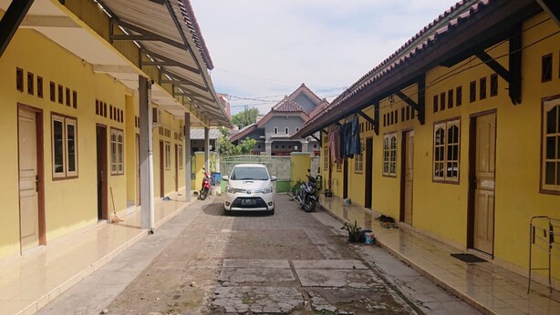 A narrow street with yellow buildings, a white car parked in the middle, and a motorcycle on the right. - SPOT ON 93005 Berkah Kedawung Syariah Near Fakultas Farmasi Universitas Muhammadiyah Ahmad Dahlan Cirebon (West Cirebon)
