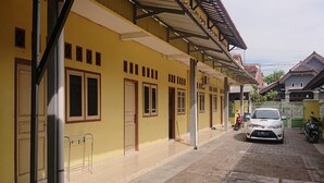 A yellow building with multiple doors and windows, a paved walkway, and a parked car. - SPOT ON 93005 Berkah Kedawung Syariah Near Fakultas Farmasi Universitas Muhammadiyah Ahmad Dahlan Cirebon (West Cirebon)