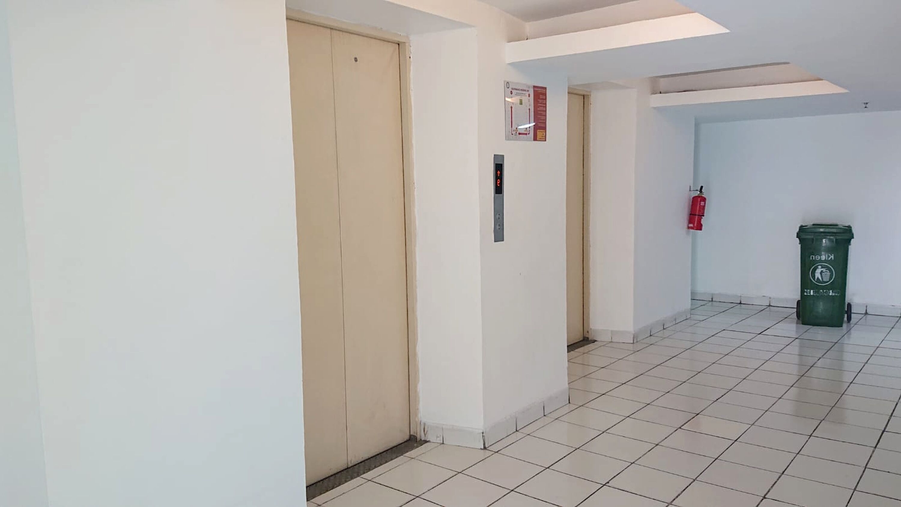 A hallway with a wooden door, a fire extinguisher, and a green recycling bin.