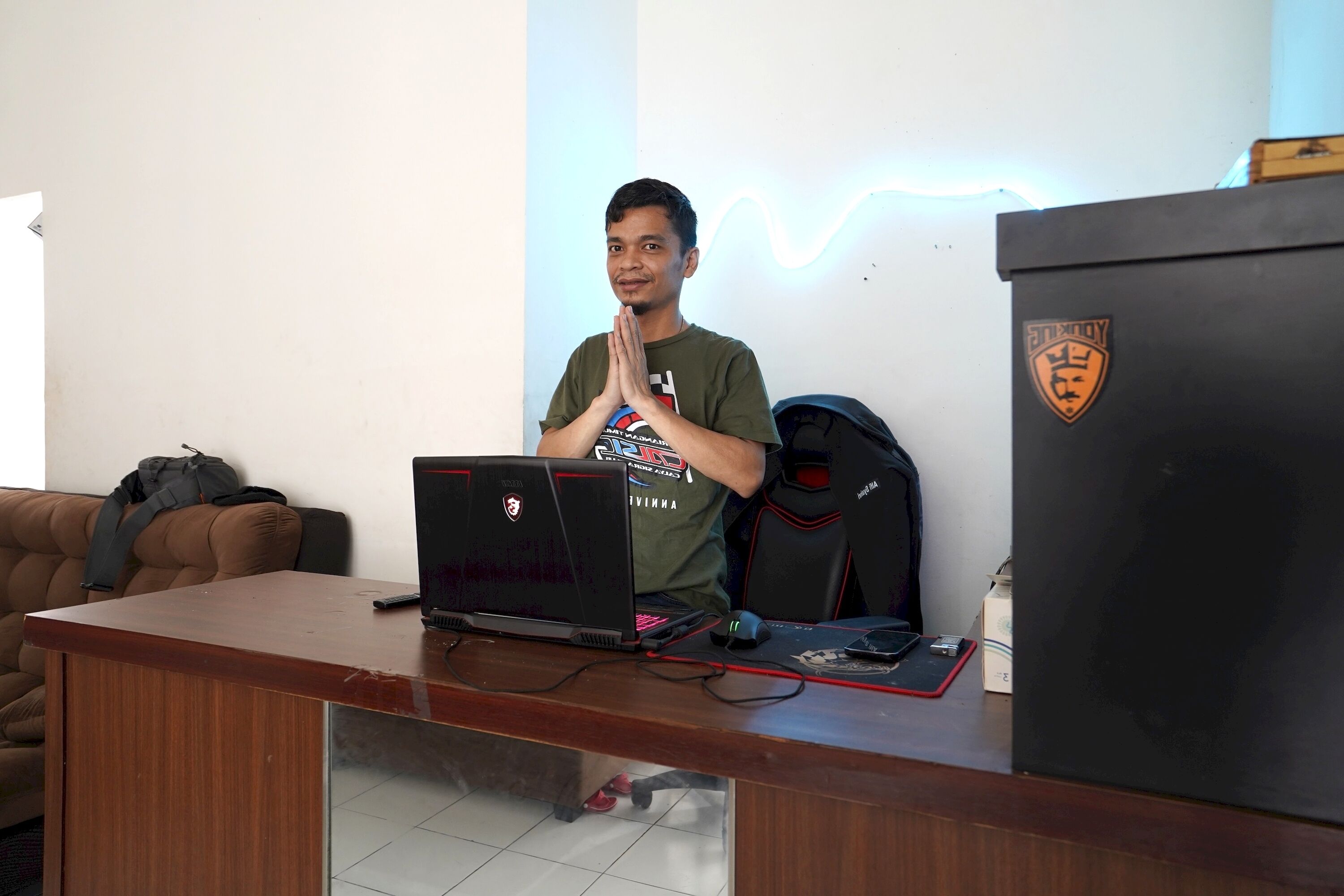 A person seated at a desk with a laptop, a gaming chair, and a gaming mouse.