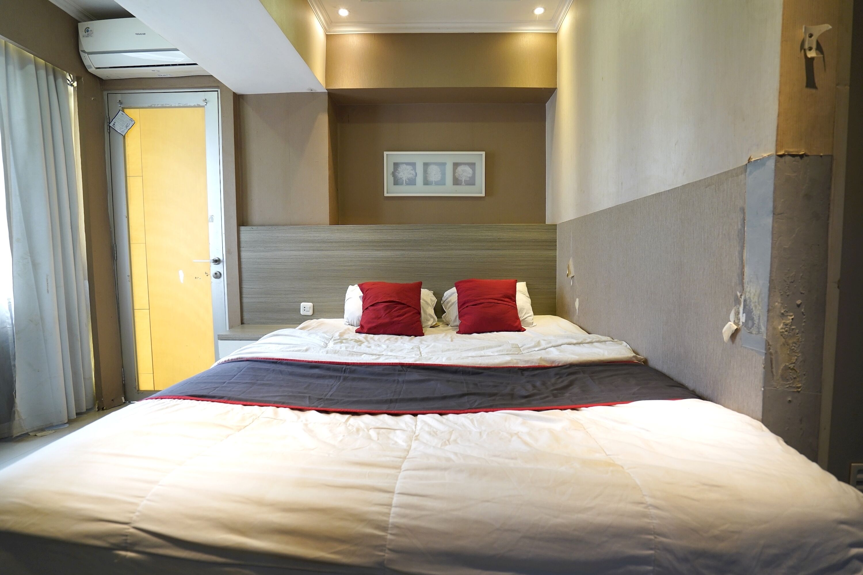 A hotel room with a large bed, a headboard, and a wall-mounted air conditioner.