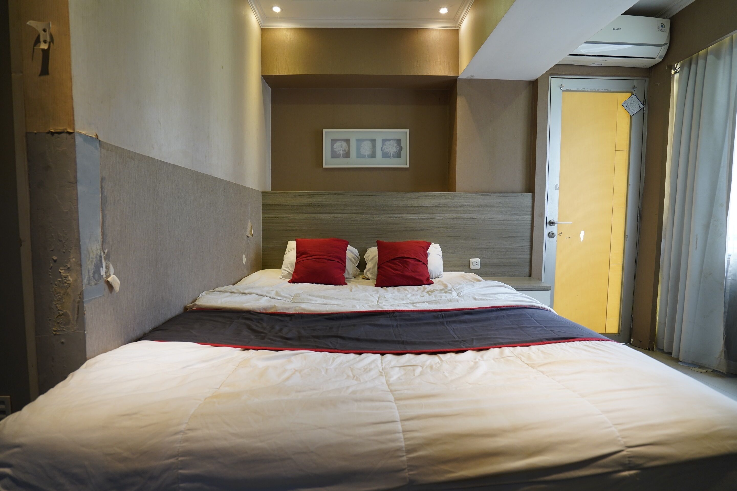 A hotel room with a bed, a door, and a wall-mounted air conditioner.
