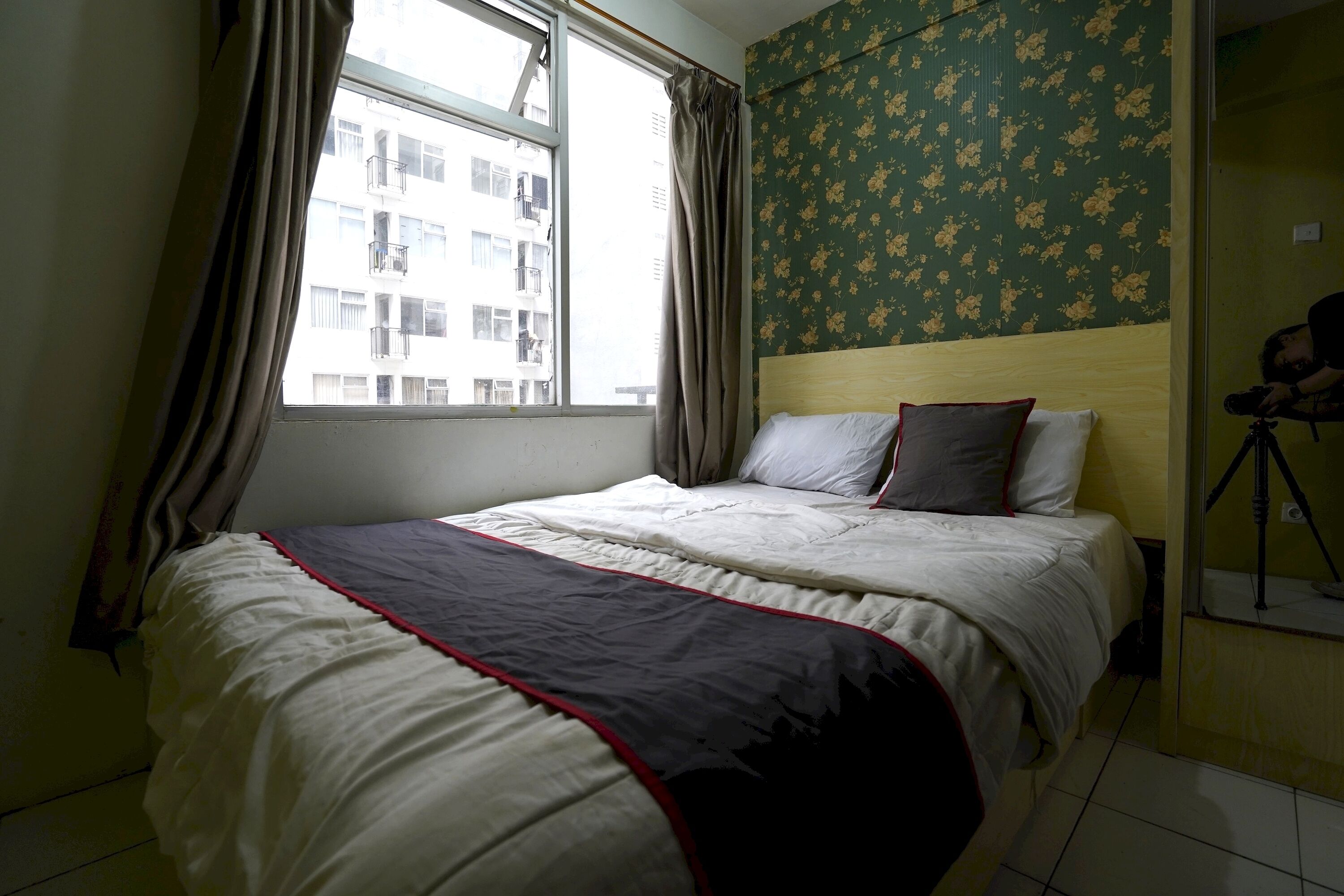 A bedroom with a bed, curtains, a window, and a floral wallpaper.