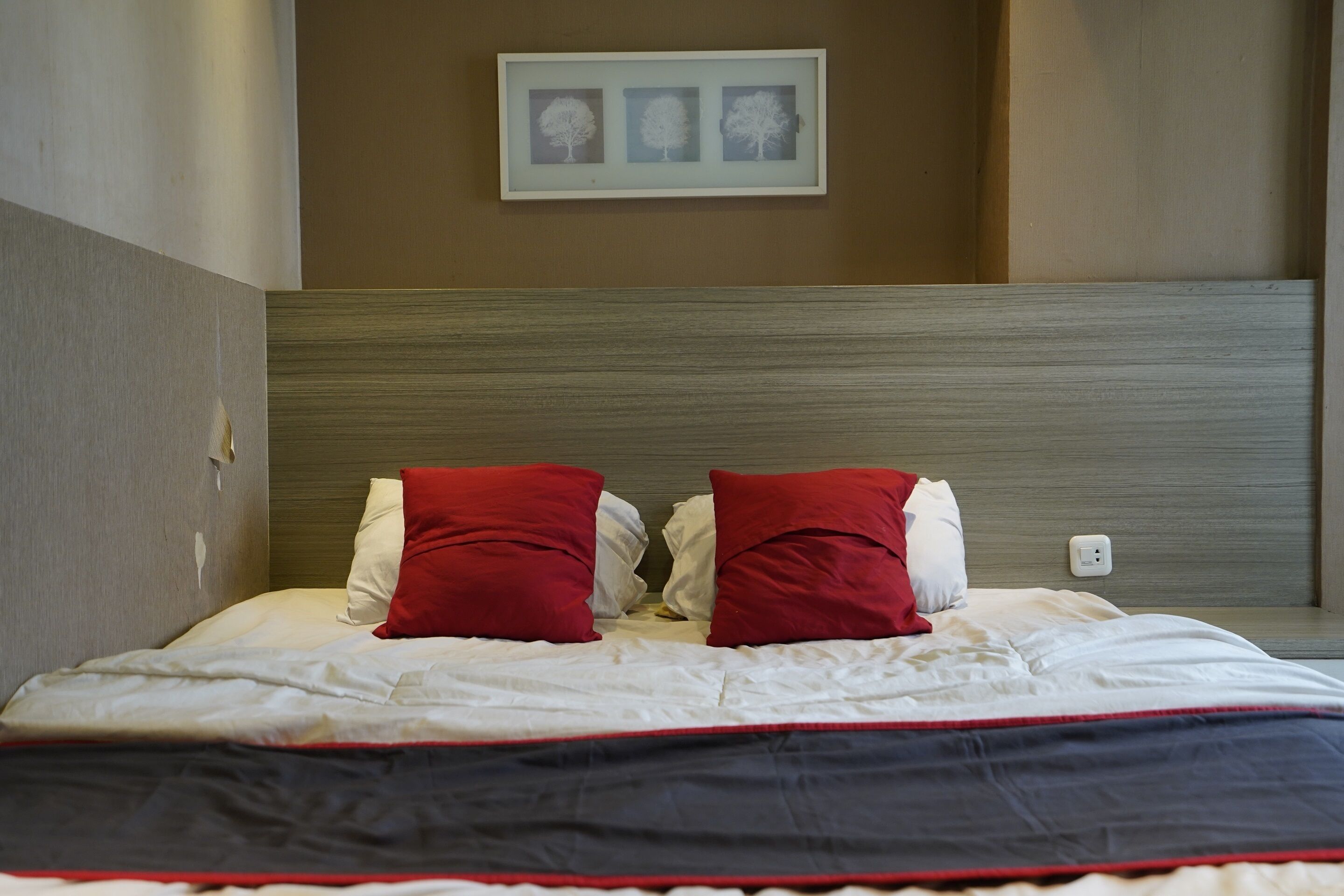 A neatly made bed with white and red bedding, a headboard with a textured design, and a framed picture on the wall above.