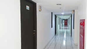 A long, narrow hallway with a tiled floor and a dark door on the left. - Collection O 92981 Apartemen The Jarrdin By Gold Suites PropertyNearSTEI ITB: Sekolah Teknik Elektro dan Informatika ITB (Bandung)