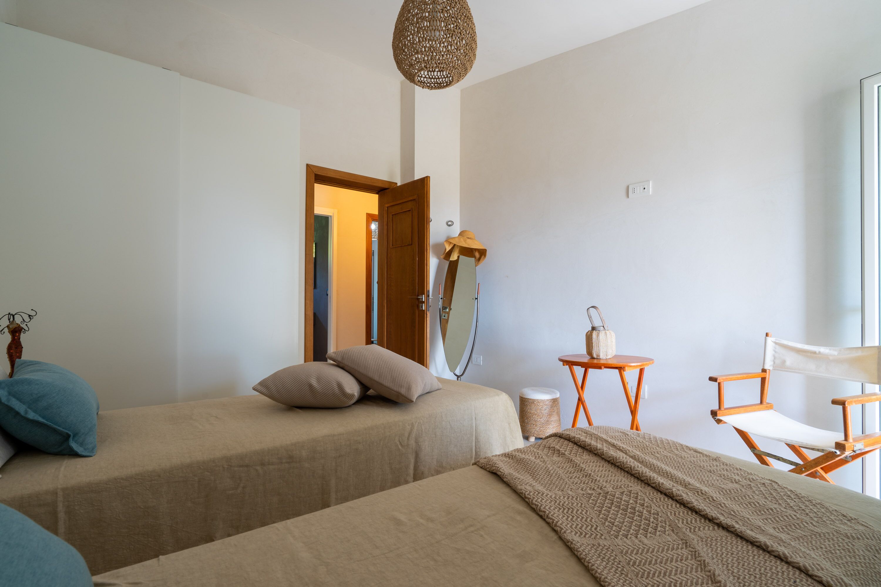 Une chambre avec deux lits, une chaise en bois, une petite table et un miroir.
