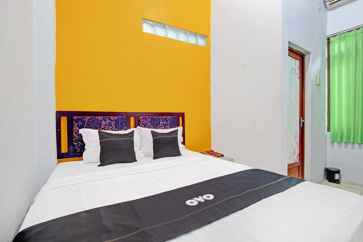 A bed with a white and black bedspread, a headboard with a colorful pattern, and a small window above the bed.