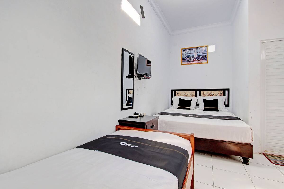 A hotel room with two beds, a TV, a small table, and a calendar on the wall.