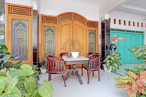 A traditional wooden door with intricate designs, a round table with chairs, and potted plants around the area. - Capital O 92929 Hotel New Tirta Kencana Syariah (Tegal)