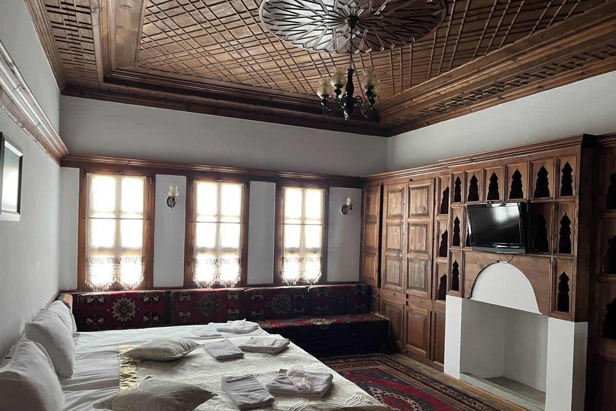 A traditional room with a wooden ceiling, a large bed with pillows and folded towels, a bench, and a television on a cabinet.