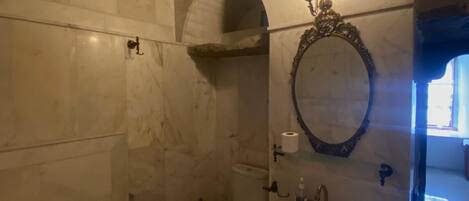 A bathroom with a marble floor, a pedestal sink, a toilet, and a mirror with an ornate frame.