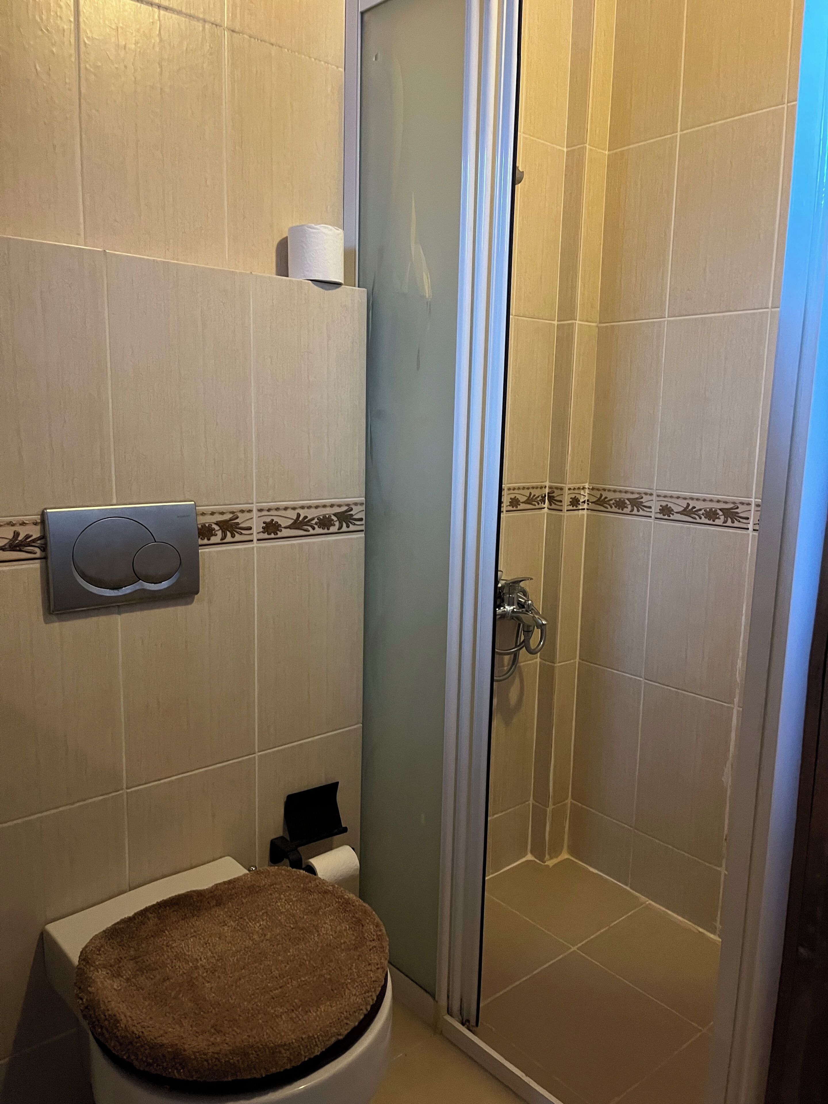 A bathroom with a toilet, a paper towel dispenser, and a glass-enclosed shower area.