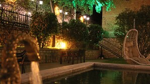 Un'area esterna illuminata di notte con piscina, posti a sedere e un'amaca.