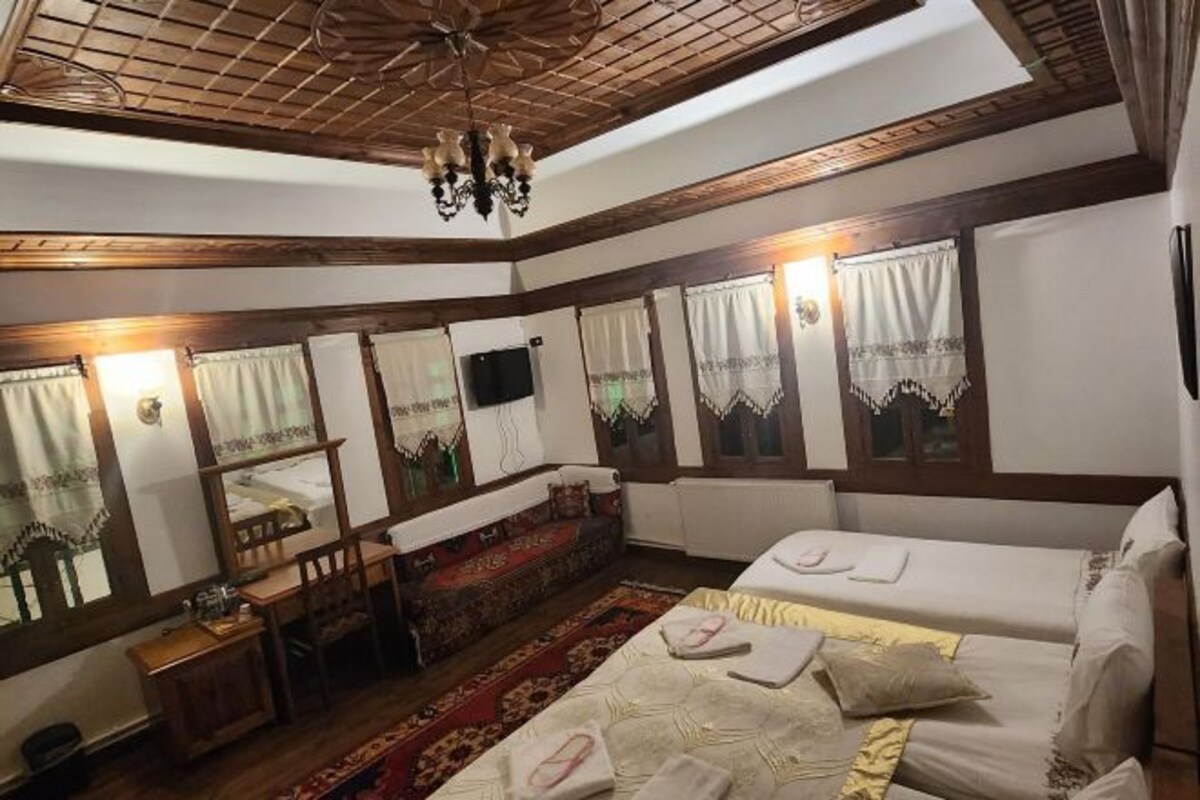 Una habitación tradicional con techo de madera, cama con ropa blanca, un sofá, una mesita y un televisor.