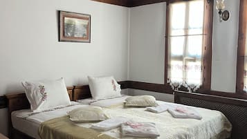 A bedroom with a wooden bed, a window with curtains, a bedside table, and a small rug.