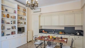 A compact kitchen with white cabinetry, a dining table with chairs, and a bookshelf filled with books and decorative items. - Lovely 1-bed Apartment in Venezia (Venice)
