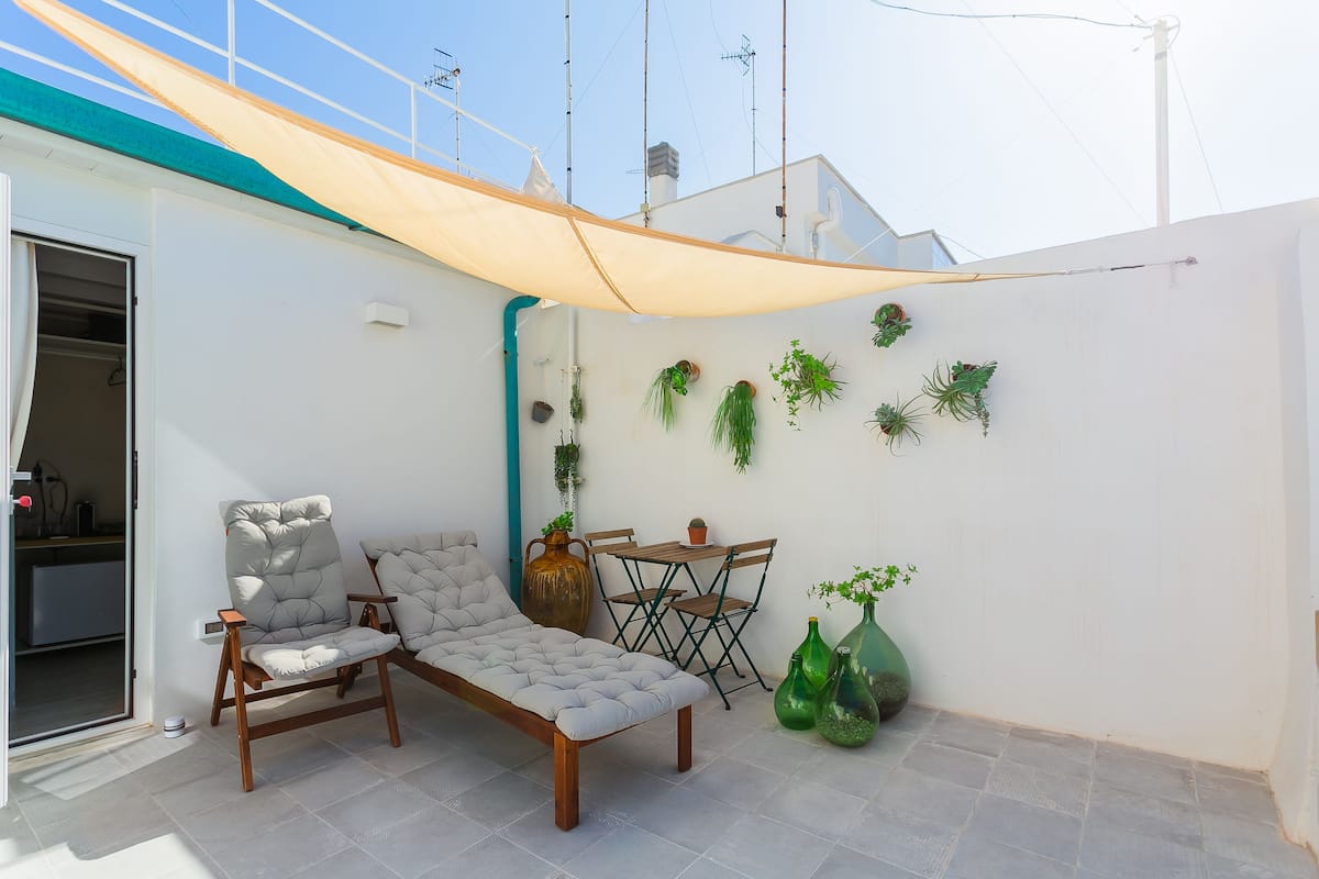 Un patio con sofá, sillas, una mesa y plantas en macetas.