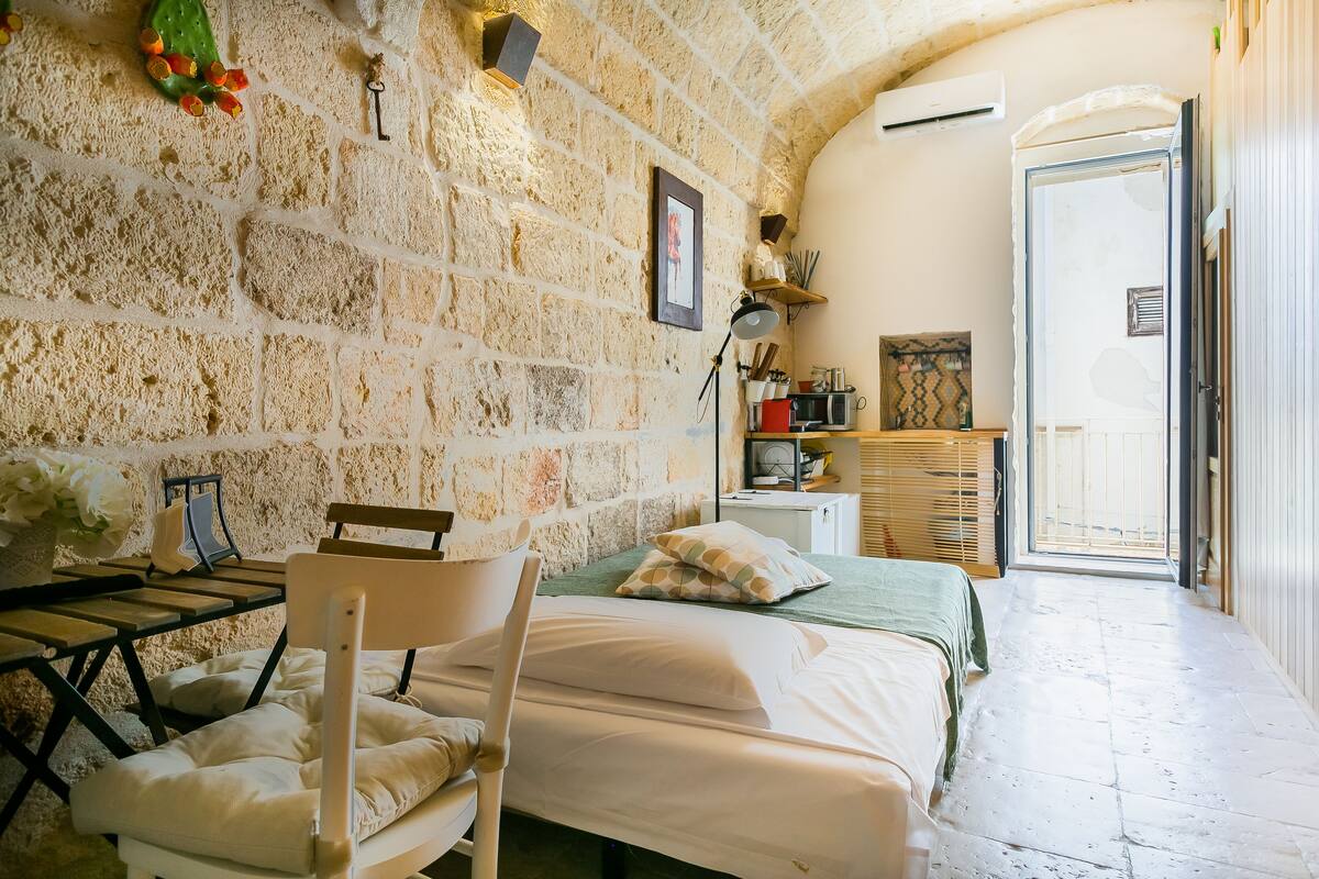 Habitación acogedora con pared de piedra, cama, silla, mesa y puerta que da a un balcón.