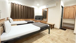 A hotel room with two beds, a television, a mirror, an air conditioning unit, and wooden cabinets. - Hotel Rajdhani (Latur)