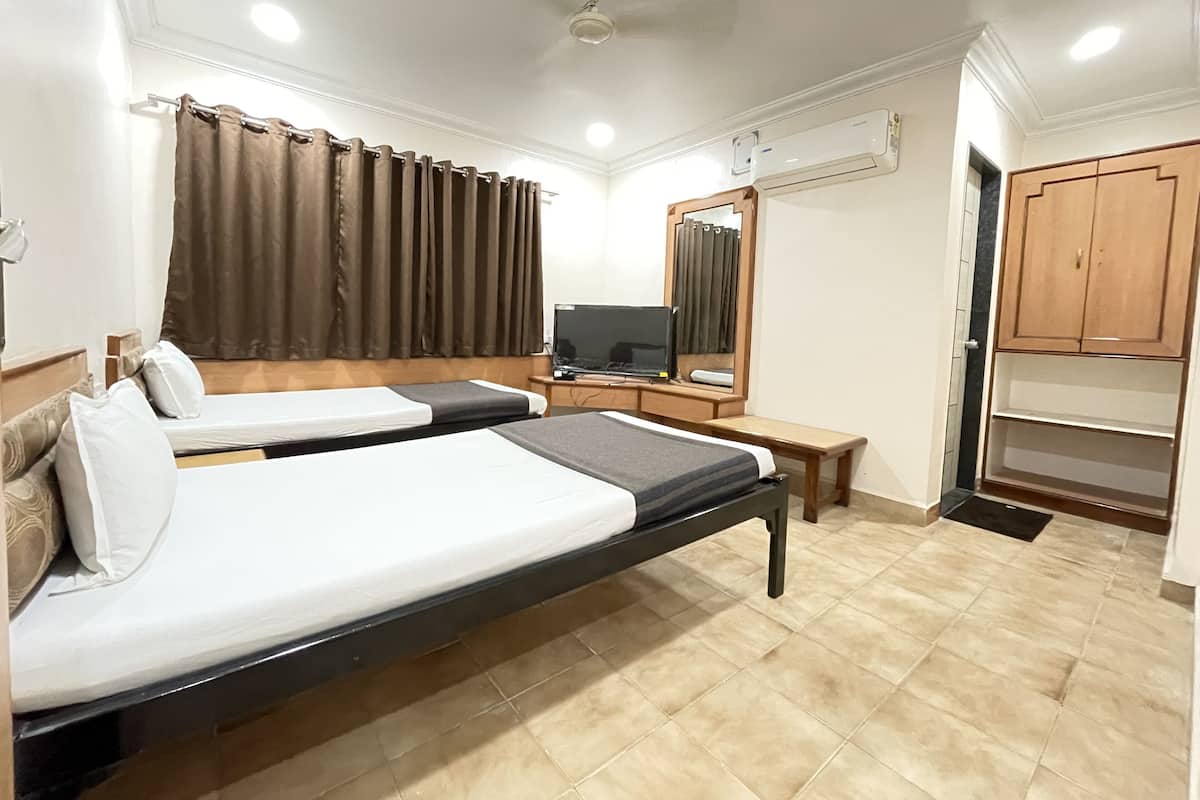 Une chambre d’hôtel avec deux lits, une télévision, un miroir, un appareil de climatisation et des armoires en bois.
