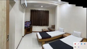 A hotel room with two beds, a TV, a small table, and a curtain. - Hotel Rajdhani (Latur)