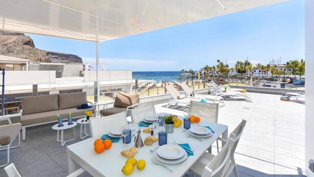 A rooftop dining area with a table set for two, overlooking a beach and marina. - Mogan Beachfront V&L by VillaGranCanaria (Mogan)