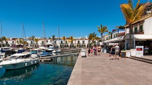 A marina with boats docked, a clear blue sky, and a pedestrian walkway with people. - Mogan Beachfront V&L by VillaGranCanaria (Mogan)