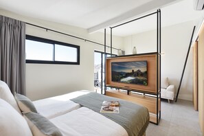 Une chambre d’hôtel moderne avec un grand lit, un téléviseur fixé sur un meuble en bois et une vue sur la ville grâce à de grandes fenêtres.