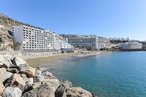 A coastal hotel with multiple buildings, a sandy beach, and rocky shoreline.