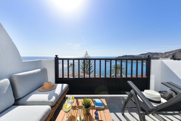 Un balcon avec un canapé, une table avec des boissons et un livre, et une vue sur la mer.