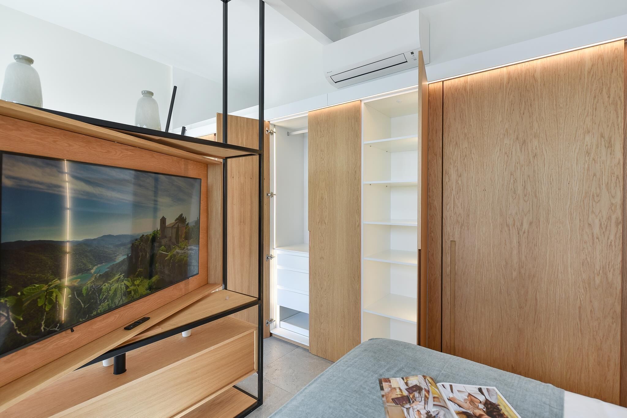Une chambre moderne dotée d’un grand téléviseur à écran plat, d’étagères en bois et d’un lit avec un présentoir à magazines.