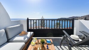Uma varanda com um sofá, uma mesa com bebidas e um livro, e vista para o mar.