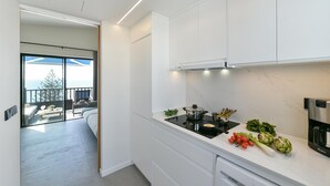 Cozinha moderna com armários brancos, bancada preta e vista para uma varanda com móveis de exterior.