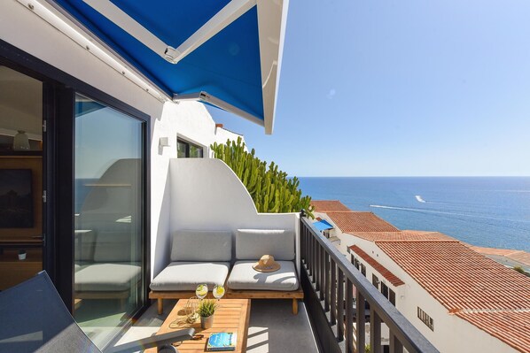 Un balcon avec un canapé blanc, une table en bois sur laquelle sont posées des boissons, et une vue sur la mer.