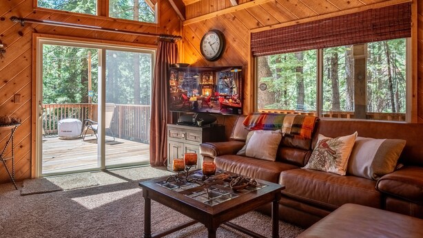 A cozy cabin interior with a wooden ceiling, a leather sofa, a coffee table, and a TV in the background. - Sukoon Retreat - Free Summer Pool Access! (Dorrington)