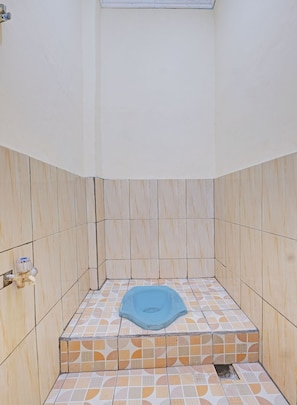 A small, tiled bathroom with a blue bathtub, wooden paneling, and a visible water spigot. - SPOT ON 92934 Nusantara Syariah (Depok)